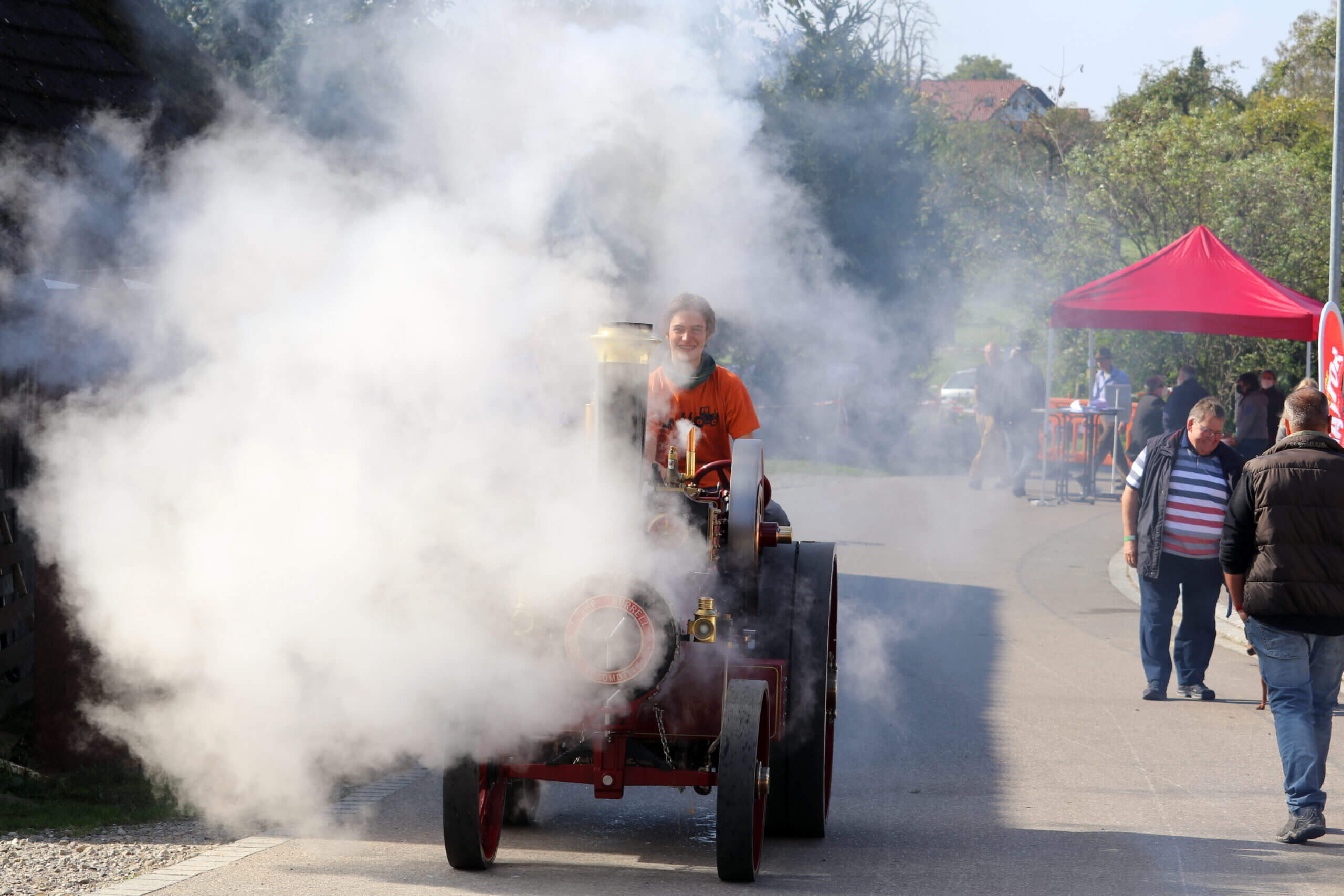 Eine kleine Dampflok fährt auf einer Straße. Überall Qualm von der Dampflok