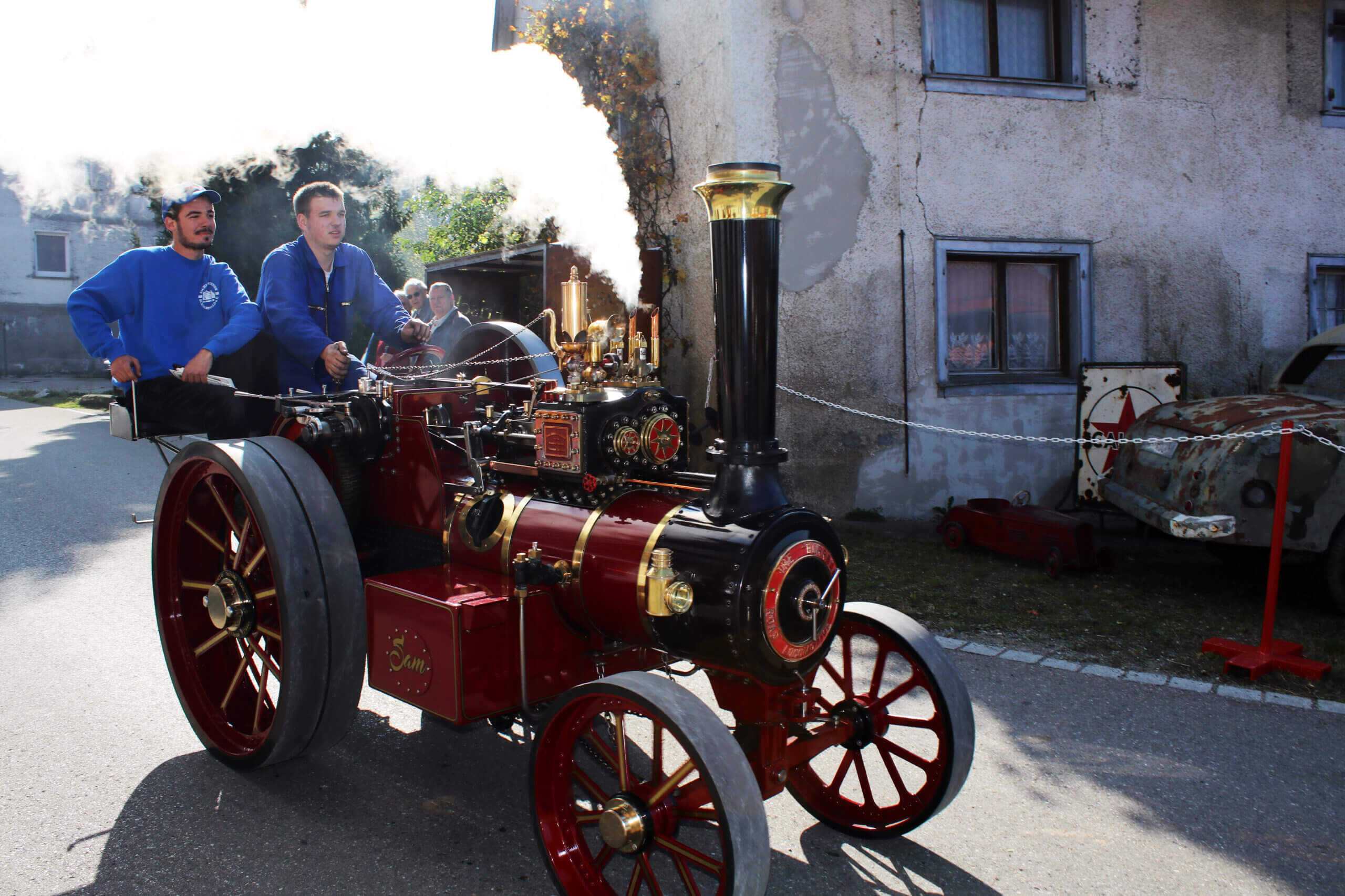 Eine kleine Dampflok fährt auf einer Straße. Überall Qualm von der Dampflok